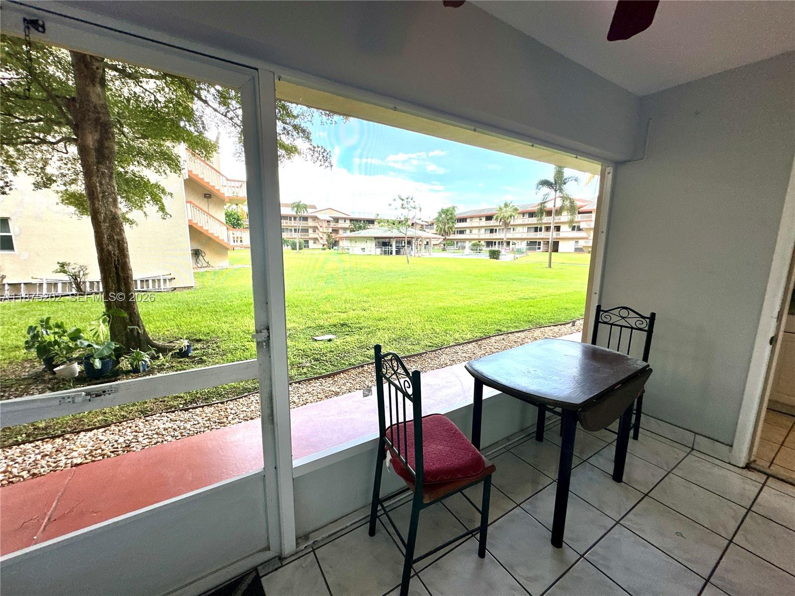 A screened-in patio with tile flooring overlooks a grassy courtyard and apartment buildings — 5300 Washington St # A139, Hollywood FL 33021, HOLLYWOOD, FL