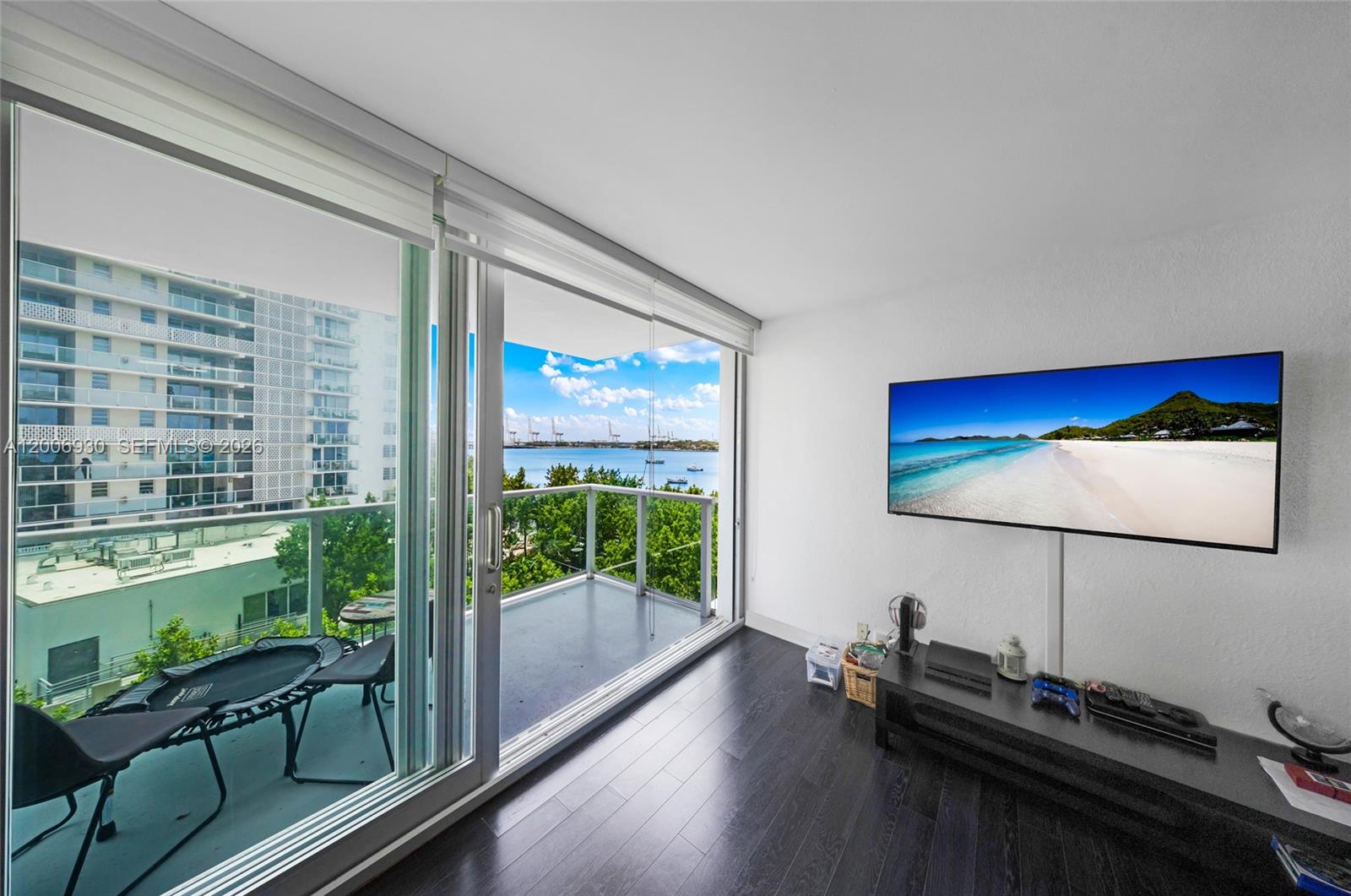A living room with dark wood floors, a wall-mounted television, and a balcony overlooking water — 1000 West Ave # 426, Miami Beach FL 33139, MIAMI BEACH, FL