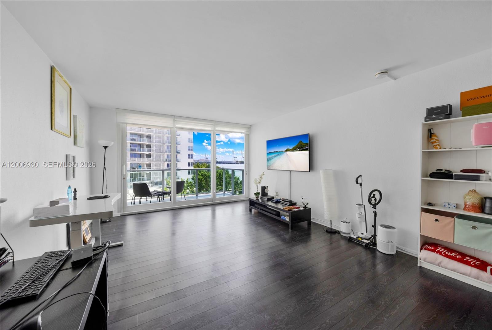A living room with dark wood floors, a wall-mounted television, and a balcony view — 1000 West Ave # 426, Miami Beach FL 33139, MIAMI BEACH, FL