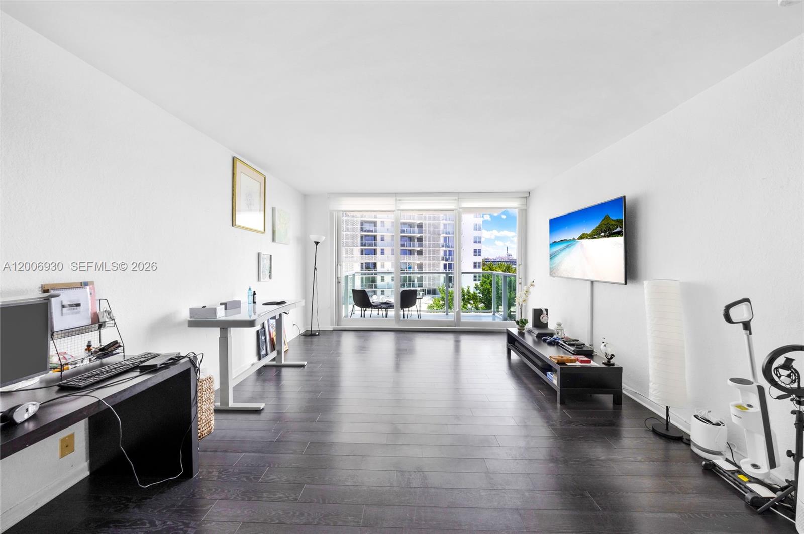 A living room features dark wood flooring, a wall-mounted television, and a balcony with seating — 1000 West Ave # 426, Miami Beach FL 33139, MIAMI BEACH, FL