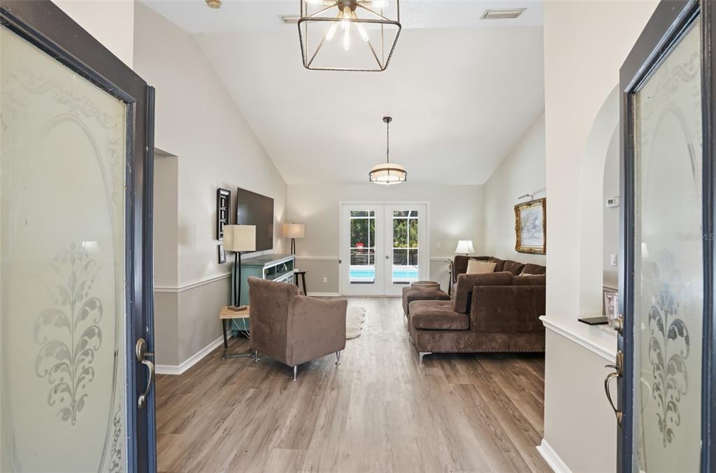 A view through an entryway into a living room with vaulted ceilings and wood flooring — 610 WOODVIEW WAY, BRADENTON, FL
