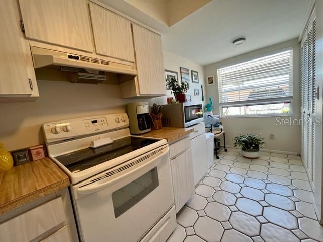 A kitchen features light wood cabinets, a white electric stove, and tiled flooring — 9616 MIDIRON COURT, NEW PORT RICHEY, FL