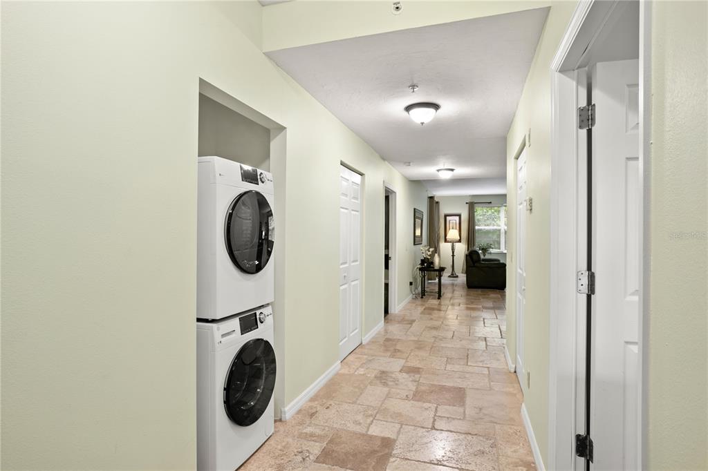 A hallway with tile flooring features a stacked washer and dryer in a recessed nook — 3506 54TH DRIVE W UNIT 108, BRADENTON, FL
