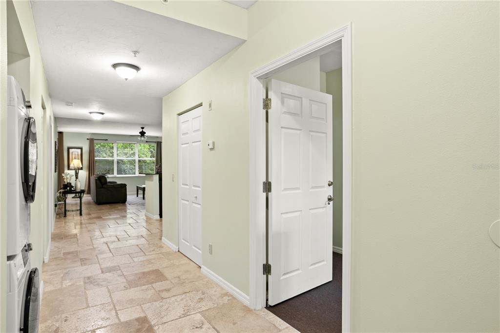 A hallway with tile flooring leads to a living area, featuring a stacked laundry unit — 3506 54TH DRIVE W UNIT 108, BRADENTON, FL