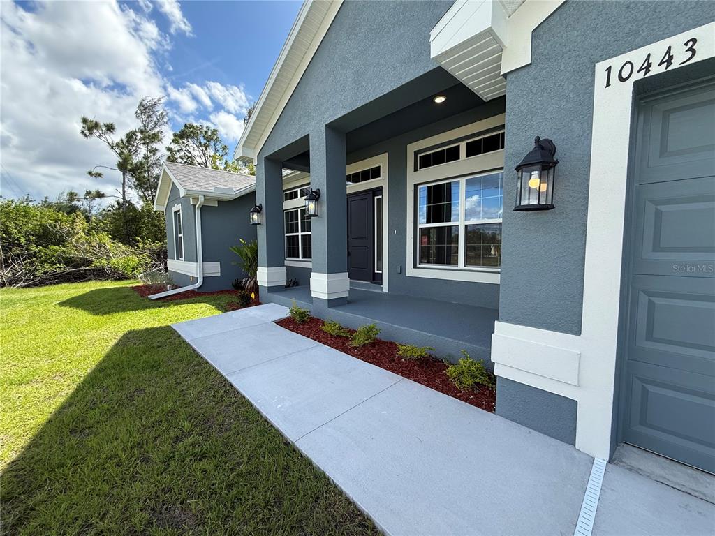 A gray house exterior features a covered porch, white trim, and a concrete walkway — 10443 SUNBURY DRIVE, PORT CHARLOTTE, FL