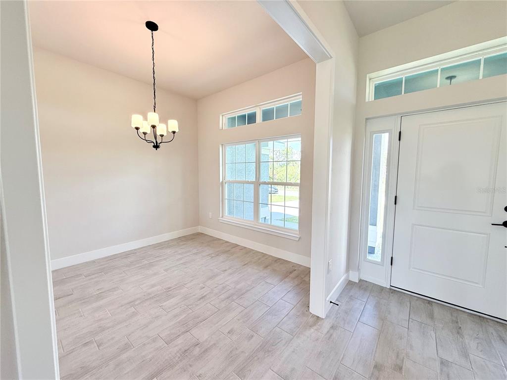A dining area features light wood-look tile flooring, a chandelier, and a white front door — 10443 SUNBURY DRIVE, PORT CHARLOTTE, FL