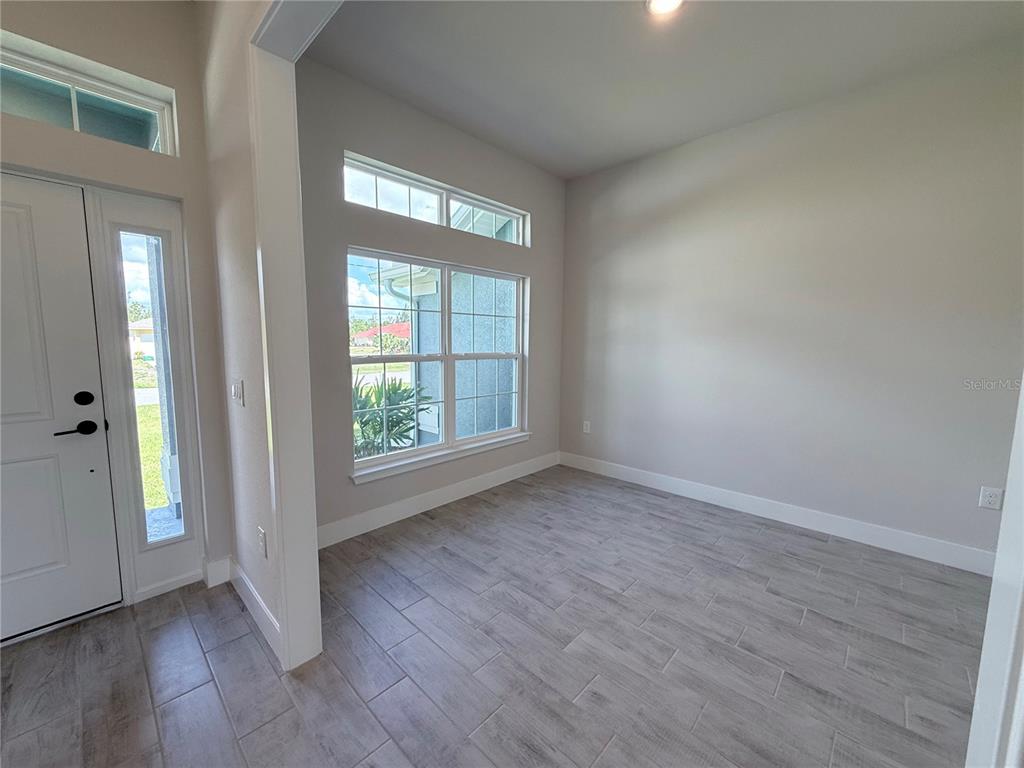 A bright room features light-colored tile flooring, neutral walls, and a large window — 10443 SUNBURY DRIVE, PORT CHARLOTTE, FL