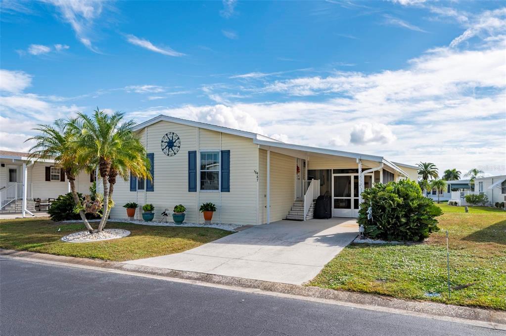 A single-story mobile home with light yellow siding, blue shutters, and a covered carport — 1000 KINGS HIGHWAY UNIT 487, PORT CHARLOTTE, FL