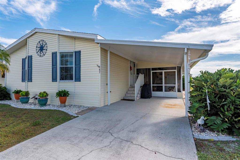 A light yellow manufactured home with blue shutters, a concrete driveway, and a covered carport — 1000 KINGS HIGHWAY UNIT 487, PORT CHARLOTTE, FL