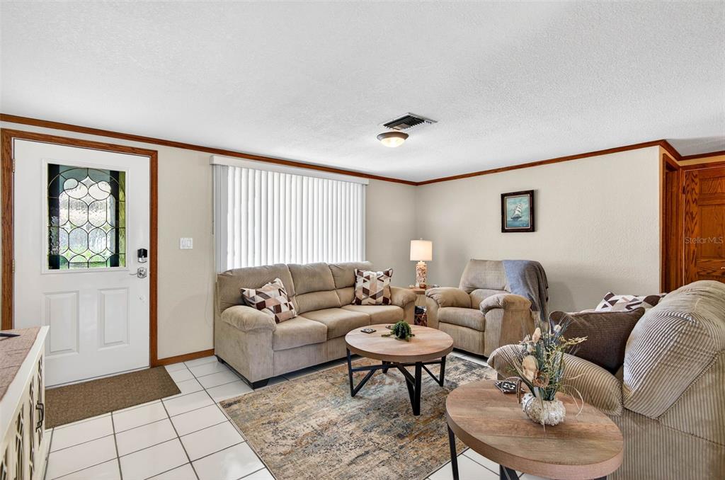 A living room features a beige sofa, two armchairs, round wooden tables, and tile flooring — 6645 HARBOR DRIVE, HUDSON, FL