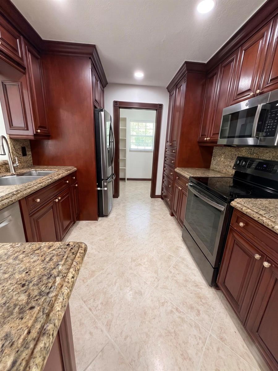 A galley kitchen features dark wood cabinets, granite countertops, stainless steel appliances, and tile flooring — 9585 Affirmed Lane, Boca Raton FL 33496, BOCA RATON, FL