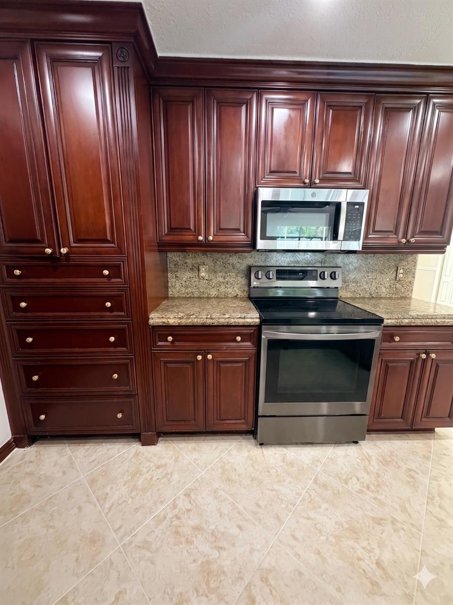 A kitchen features dark wood cabinets, stainless steel appliances, and granite countertops — 9585 Affirmed Lane, Boca Raton FL 33496, BOCA RATON, FL
