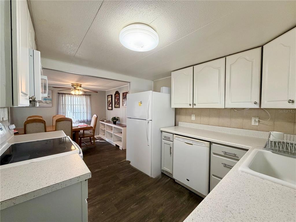 A kitchen with white cabinets and appliances opens into a dining area with wood flooring — 10399 67TH AVENUE UNIT 4, SEMINOLE, FL