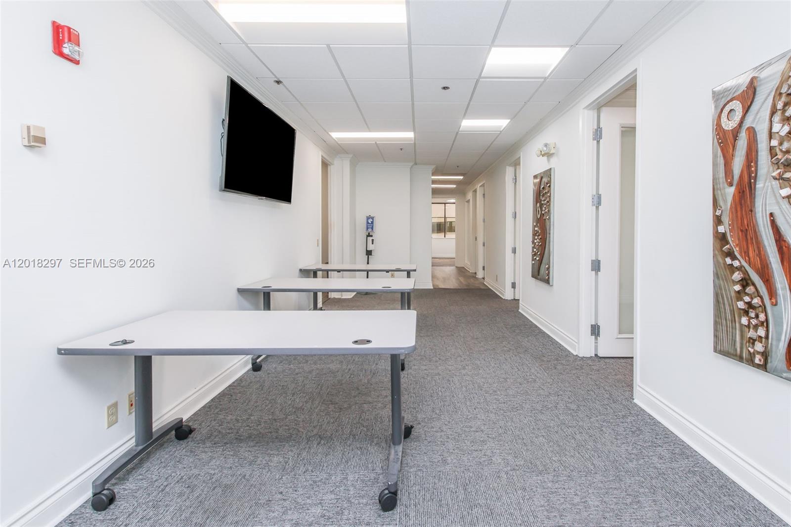 A hallway features gray carpet, white walls, three rolling tables, and wall-mounted artwork — 1900 Glades Rd # 301, Boca Raton FL 33431, BOCA RATON, FL
