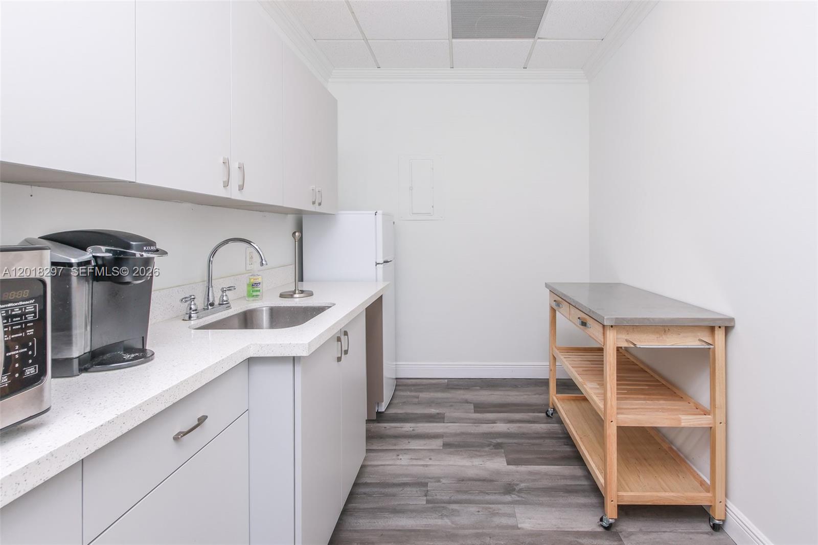 A small kitchen features white cabinets, a stainless steel sink, and a wooden rolling cart — 1900 Glades Rd # 301, Boca Raton FL 33431, BOCA RATON, FL
