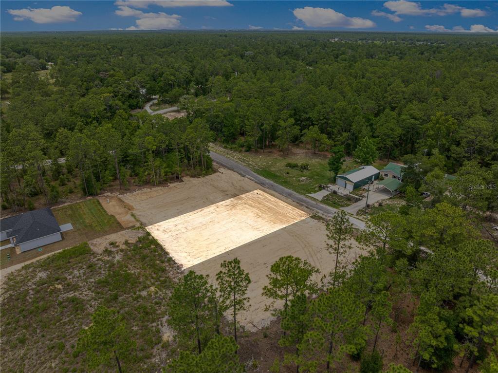 An aerial view shows a cleared, rectangular residential lot surrounded by trees and nearby houses — SW 38TH PLACE, OCALA, FL