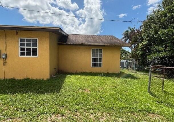 The exterior of a yellow stucco house features two windows and a shingled roof — 943 DELLA TOBIAS AVENUE, CLEWISTON, FL