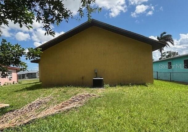 The exterior side of a yellow house features an air conditioning unit on the lawn — 943 DELLA TOBIAS AVENUE, CLEWISTON, FL