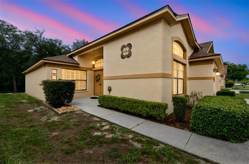 A single-story house with a tan stucco exterior, a brown shingled roof, and landscaped bushes — 9311 HAAS DRIVE, HUDSON, FL