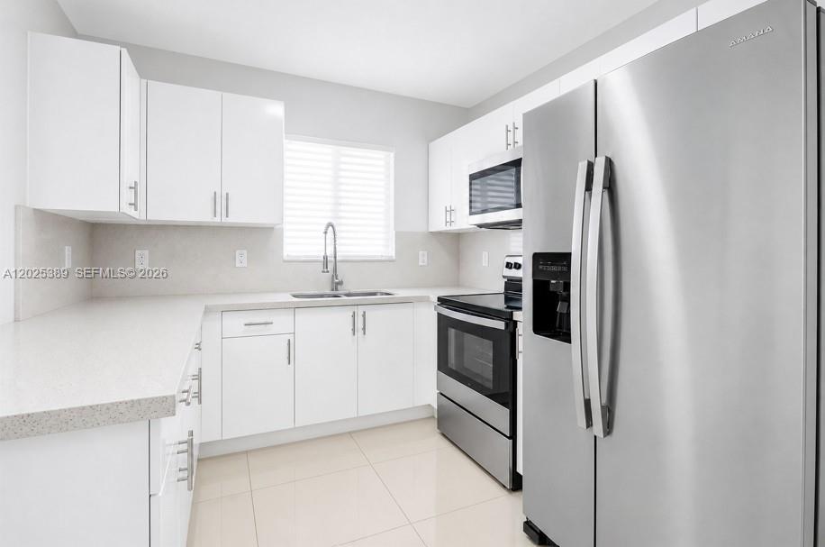 A modern kitchen features white cabinets, stainless steel appliances, and light-colored tile flooring — 1180 NW 67th St # 2, Miami FL 33150, MIAMI, FL