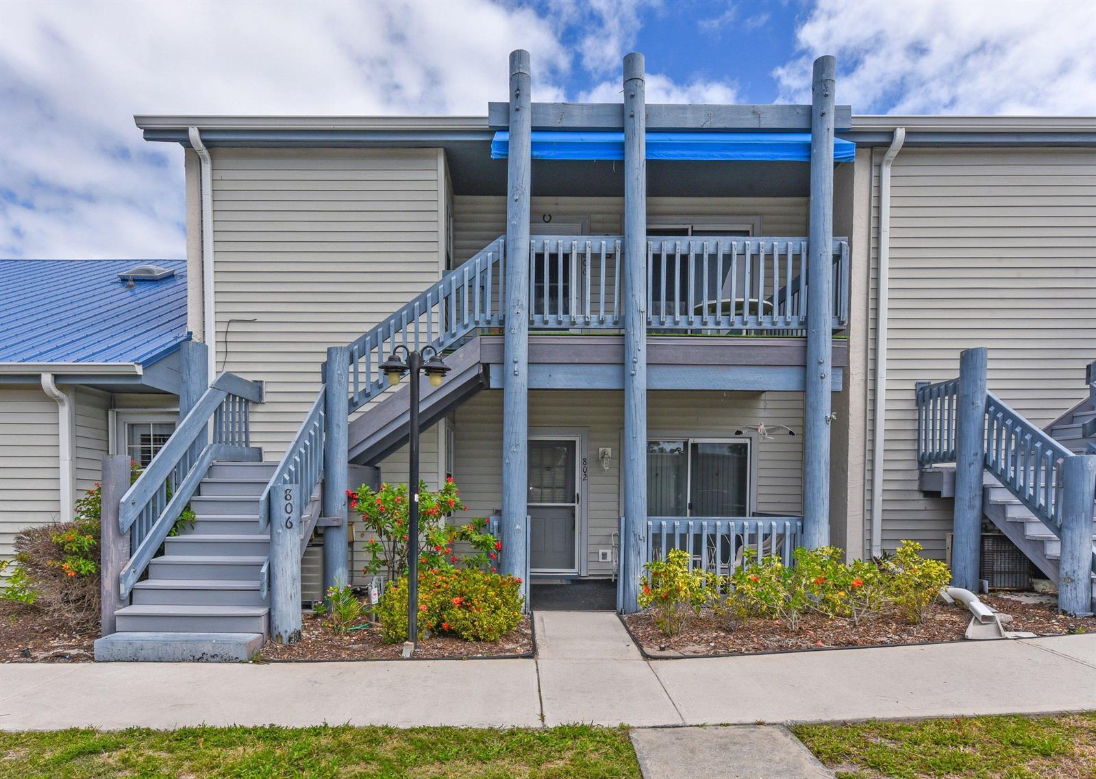A two-story apartment building exterior features gray siding, blue wooden railings, and a blue awning — 1637 NE Nautical Place # 802, Jensen Beach FL 34957, JENSEN BEACH, FL