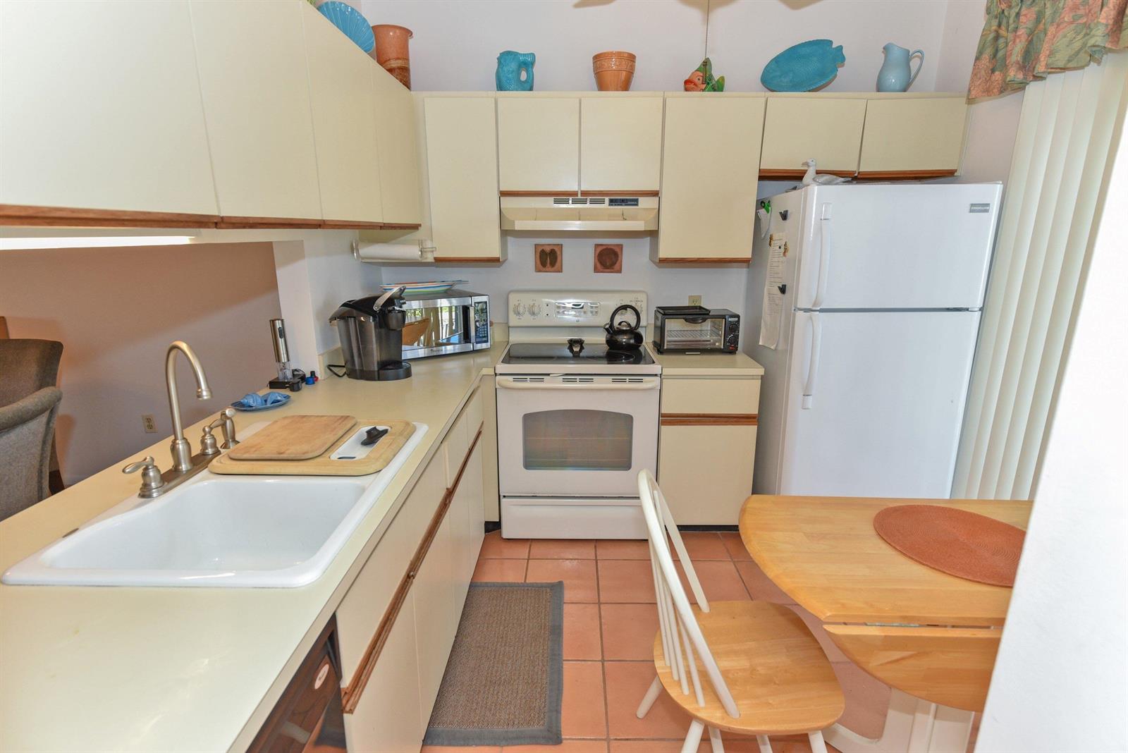 A kitchen features light-colored cabinetry, white appliances, a tiled floor, and a small dining table — 1637 NE Nautical Place # 802, Jensen Beach FL 34957, JENSEN BEACH, FL