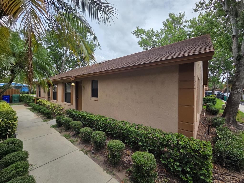 A tan exterior wall of a single-story building features a sidewalk and manicured hedges — 320 ERON WAY UNIT 6, WINTER GARDEN, FL