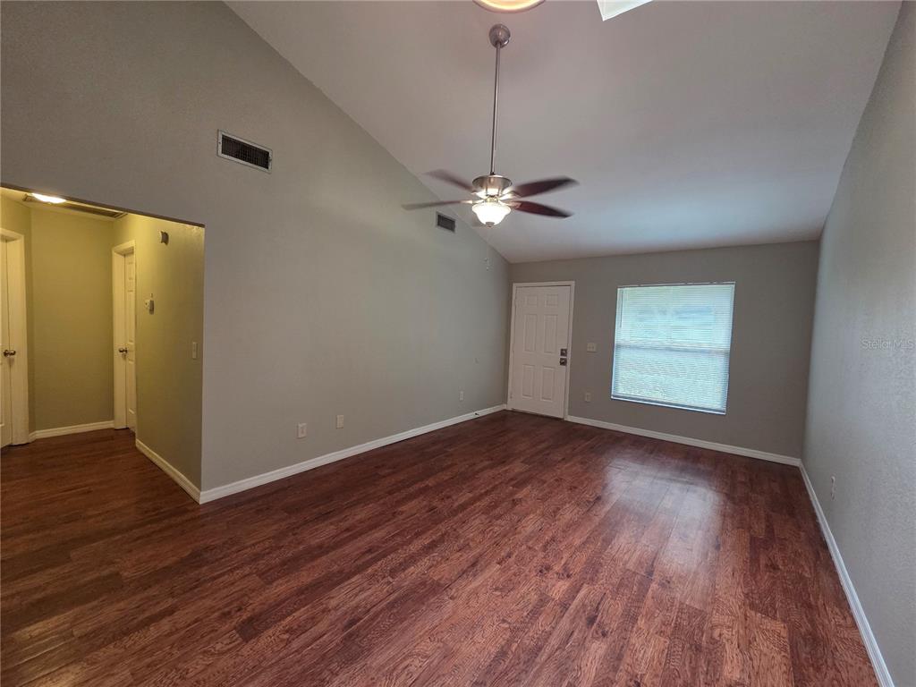 An empty living room features vaulted ceilings, a ceiling fan, and wood-look laminate flooring — 320 ERON WAY UNIT 6, WINTER GARDEN, FL