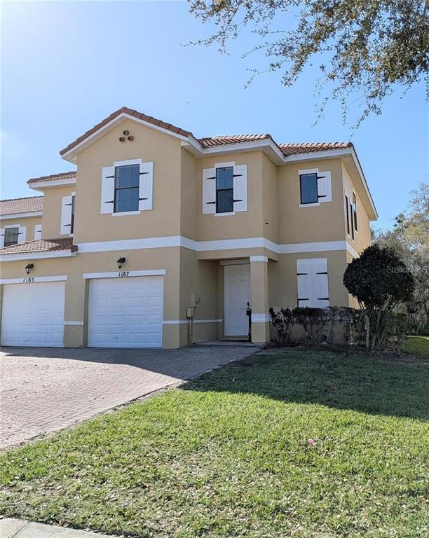 A two-story tan stucco townhouse with a two-car garage and white shutters — 1326 CLOVE DRIVE, POINCIANA, FL