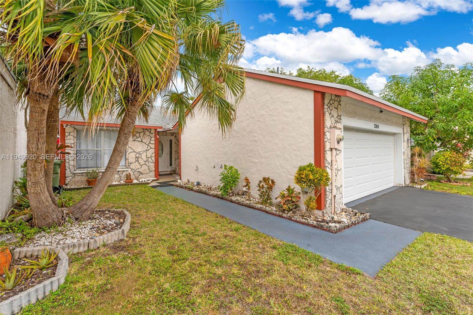 A single-story house features a stone facade, a white garage door, and a palm tree — 1304 Redstart Ct, Homestead FL 33035, HOMESTEAD, FL