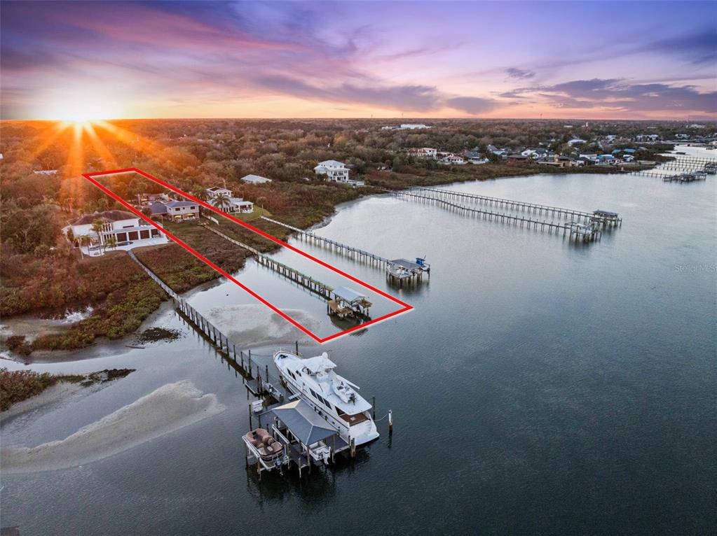 An aerial view shows a waterfront property with a long dock and a large yacht — 1703 S RIVERSIDE DRIVE, NEW SMYRNA BEACH, FL