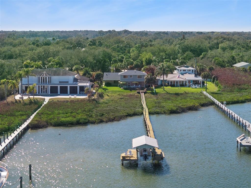 An aerial view shows three waterfront houses with private docks extending into the river — 1703 S RIVERSIDE DRIVE, NEW SMYRNA BEACH, FL