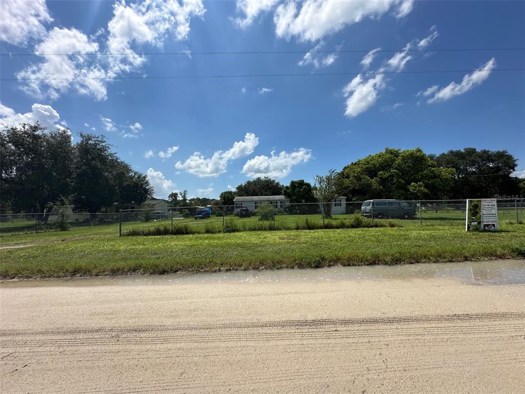 A fenced, grassy lot with a mobile home and a for-sale sign under a blue sky — 8747 MCKENDREE ROAD, WESLEY CHAPEL, FL