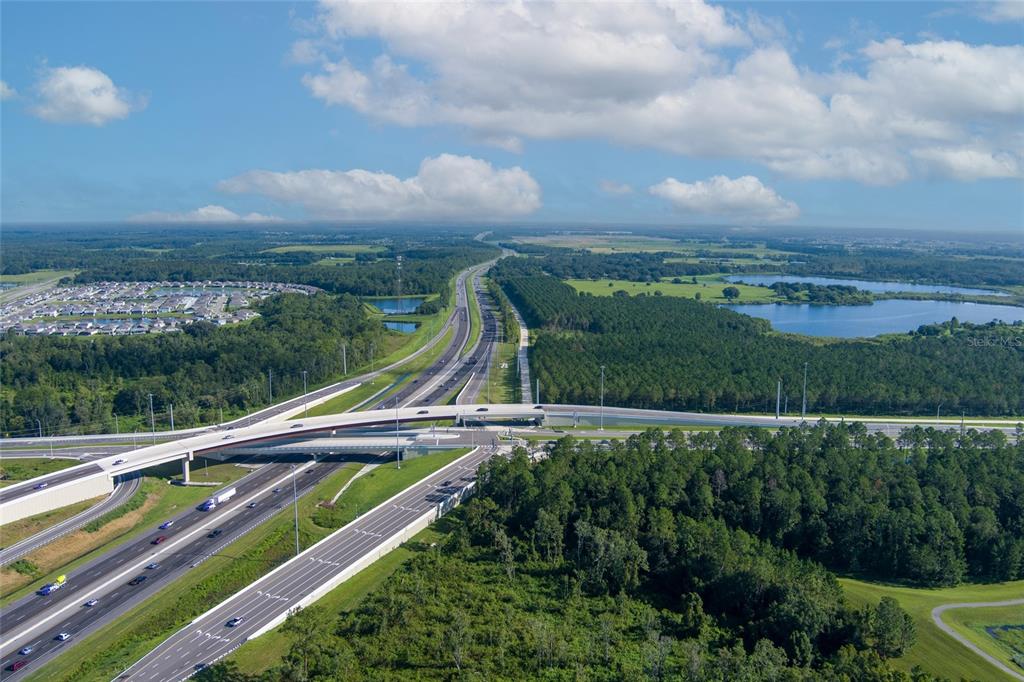 An aerial view shows a highway interchange surrounded by forests, lakes, and a residential neighborhood — 8747 MCKENDREE ROAD, WESLEY CHAPEL, FL