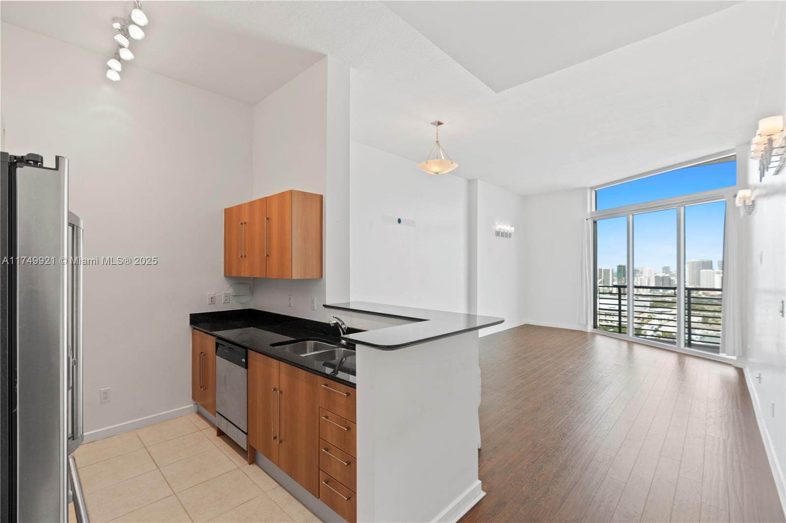 A kitchen with wood cabinets and black countertops opens into a living area with balcony — 335 S Biscayne Blvd, Miami FL 33131, MIAMI, FL