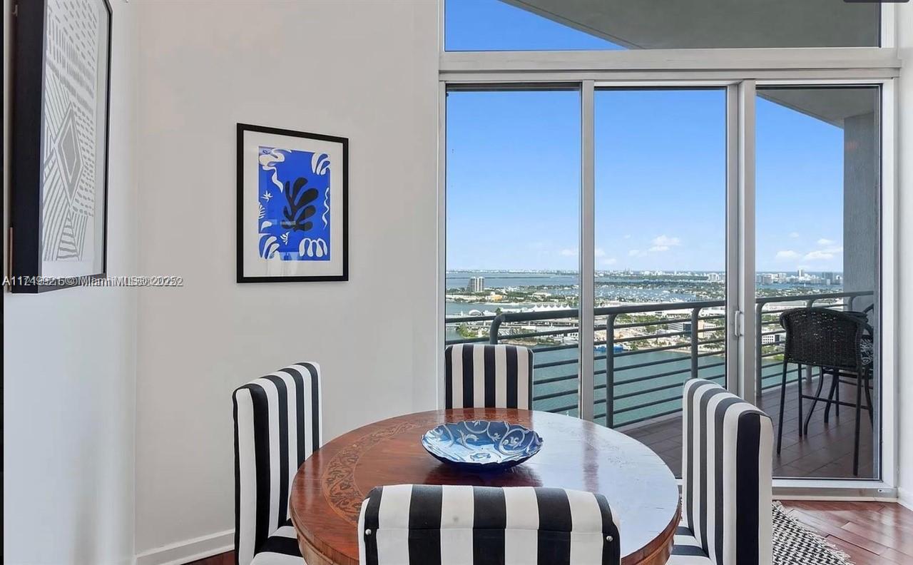 A dining area features a round wooden table, striped chairs, and a balcony with water views — 335 S Biscayne Blvd, Miami FL 33131, MIAMI, FL