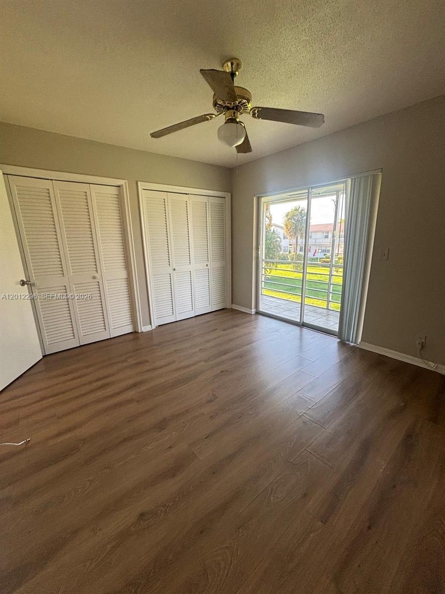 A bedroom features wood-look flooring, two sets of louvered closet doors, and a sliding glass door — WEST PALM BEACH, FL