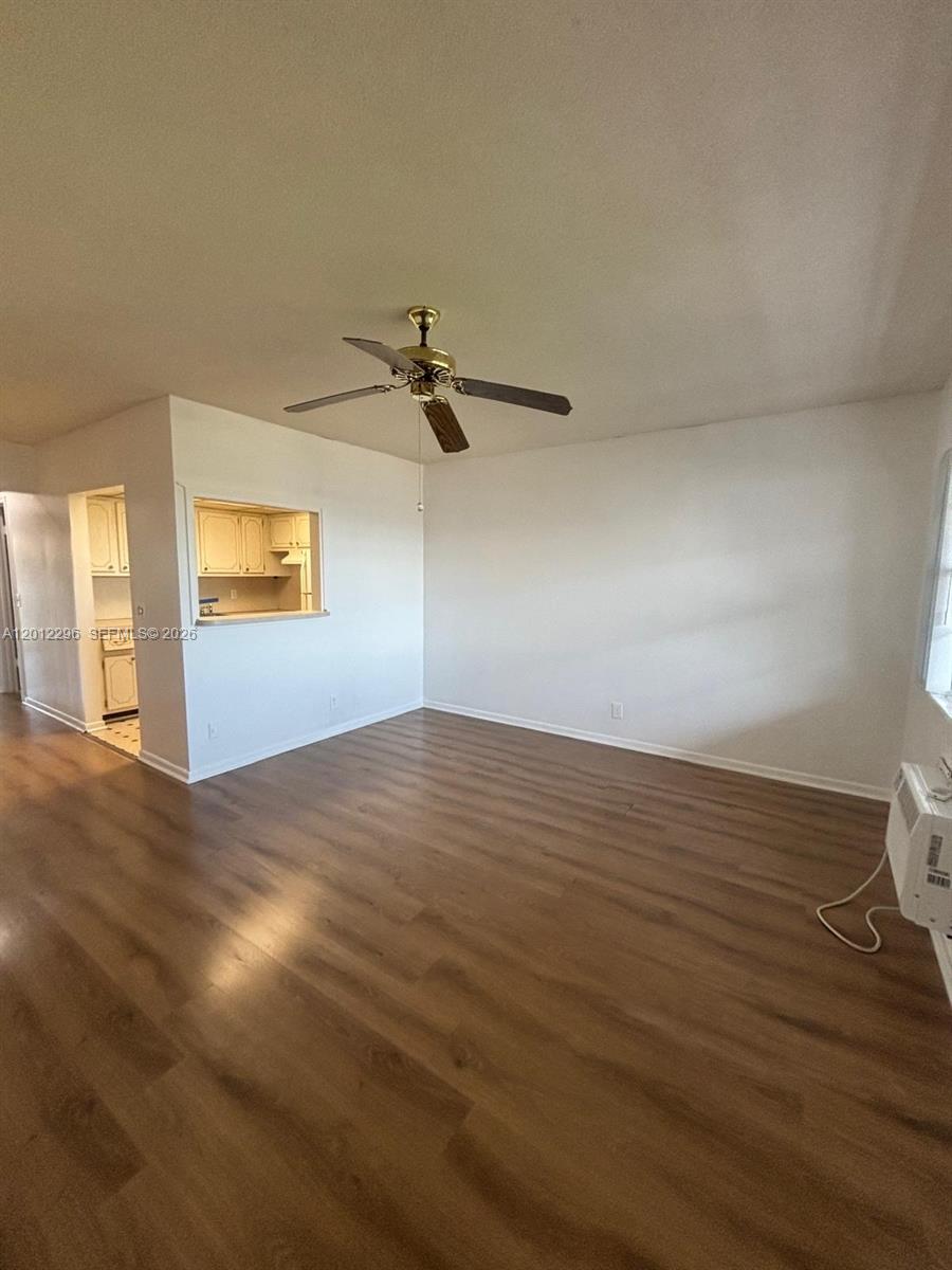 An empty living room features wood-look flooring, a ceiling fan, and a kitchen pass-through window — WEST PALM BEACH, FL