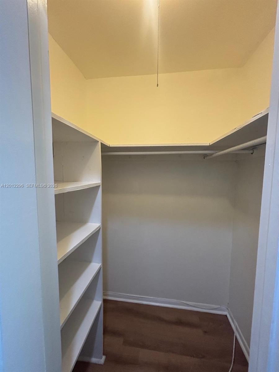 A walk-in closet features white shelving units, a hanging rod, and wood-look flooring — WEST PALM BEACH, FL