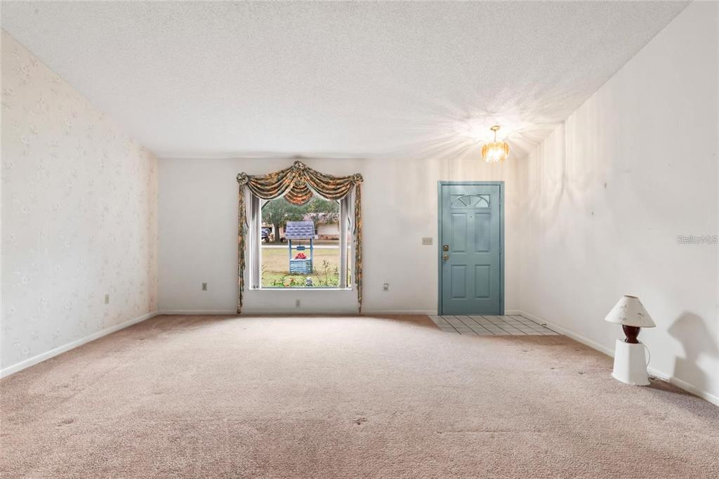 A carpeted living room features a large window with ornate valance curtains and a blue door — 5250 LITTLE GREEN LANE, DADE CITY, FL