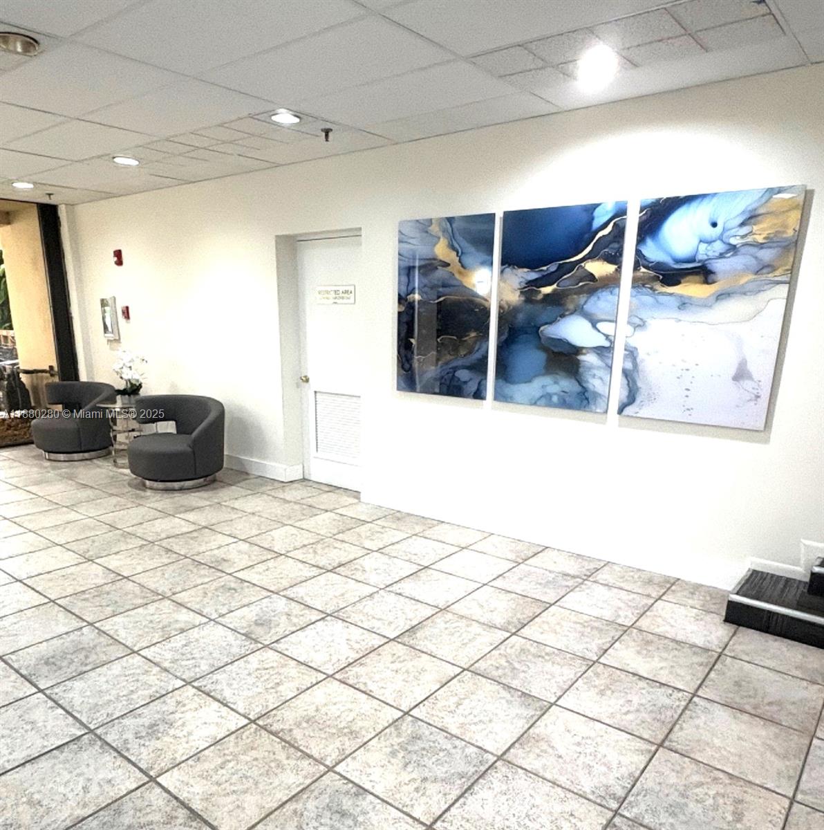 A waiting area features tiled floors, two gray armchairs, and three abstract blue-and-gold wall panels — 900 NE 195th St # 702, Miami FL 33179, MIAMI, FL