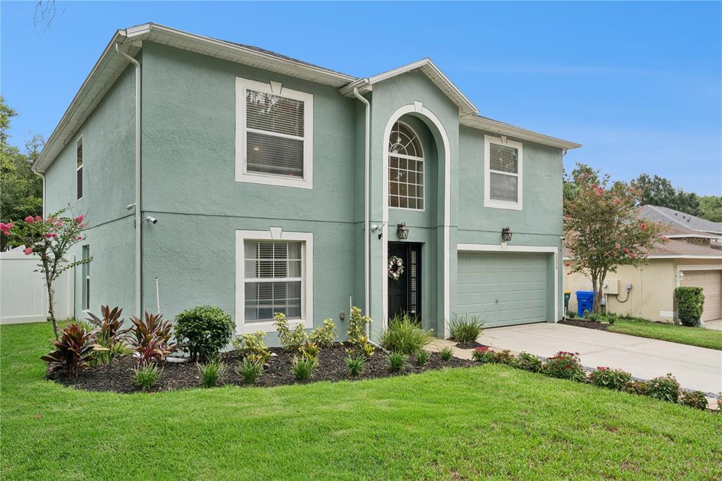 A two-story, light green stucco house features a front-facing garage and a arched entryway — 2333 FOXTREE ROAD, TAVARES, FL