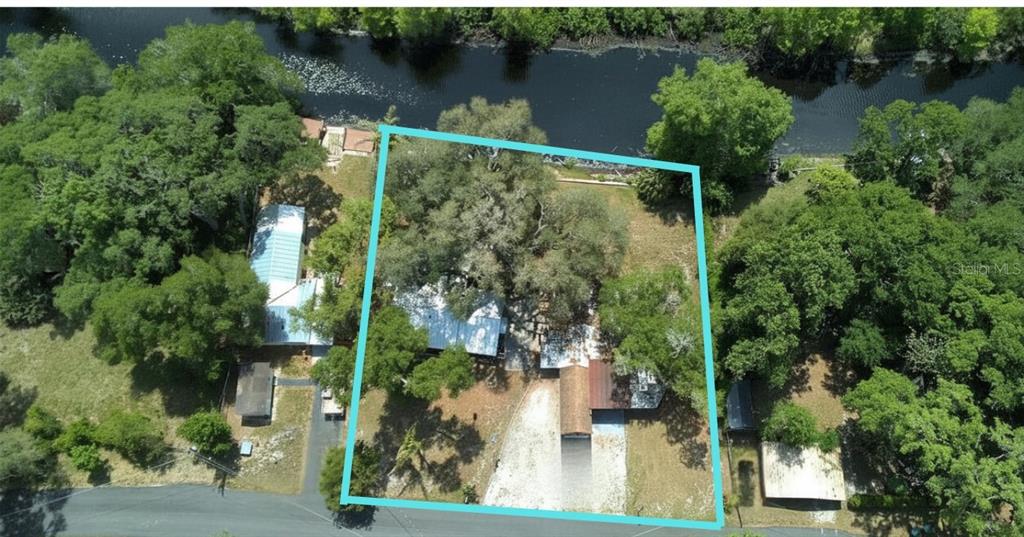 An aerial view shows a house with a metal roof situated on a wooded waterfront lot — 11717 E SALMON DRIVE, FLORAL CITY, FL