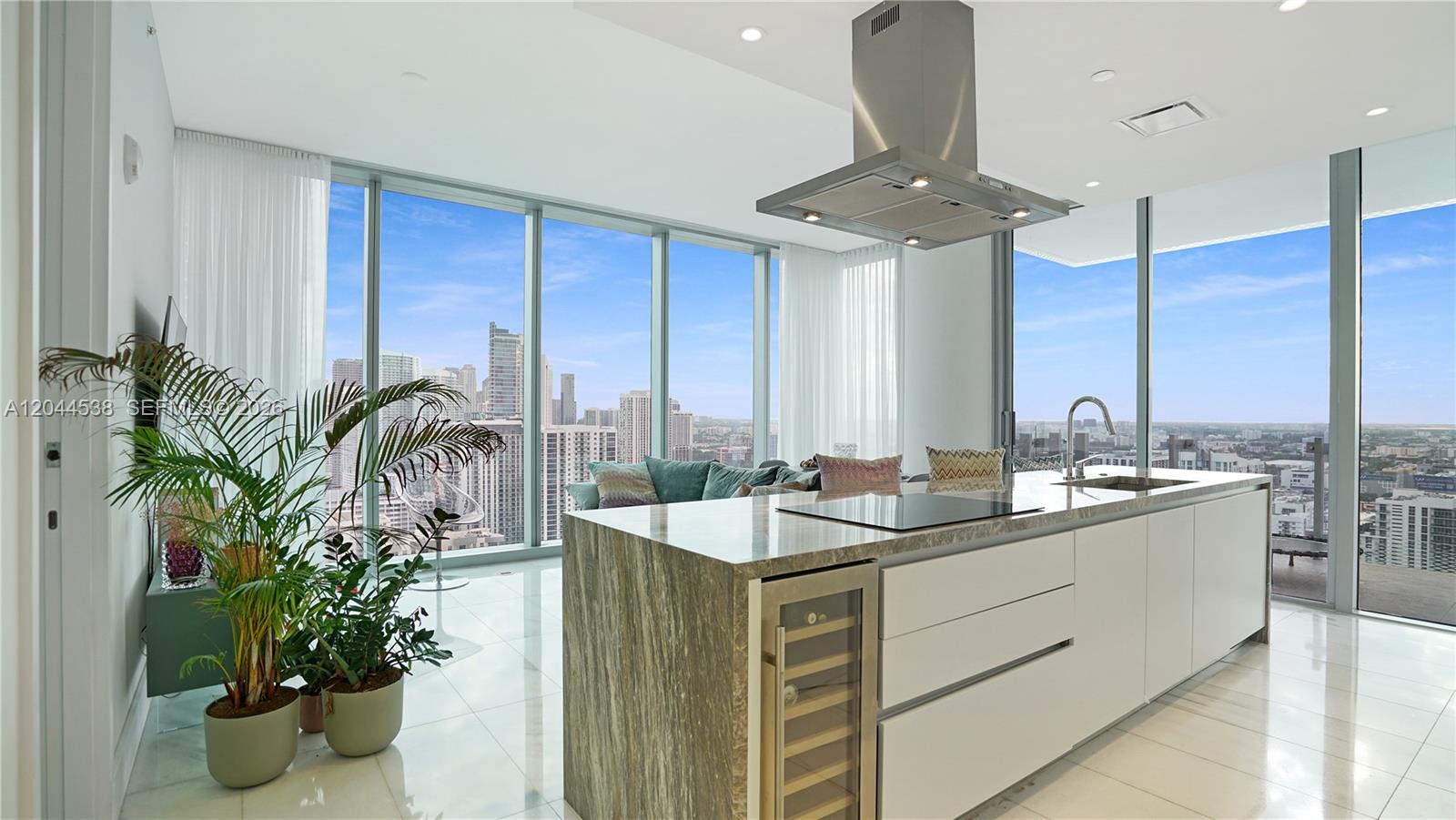 A modern kitchen with a stone-topped island and wine cooler overlooks a city skyline — 700 NE 26th Ter # 3005, Miami FL 33137, MIAMI, FL