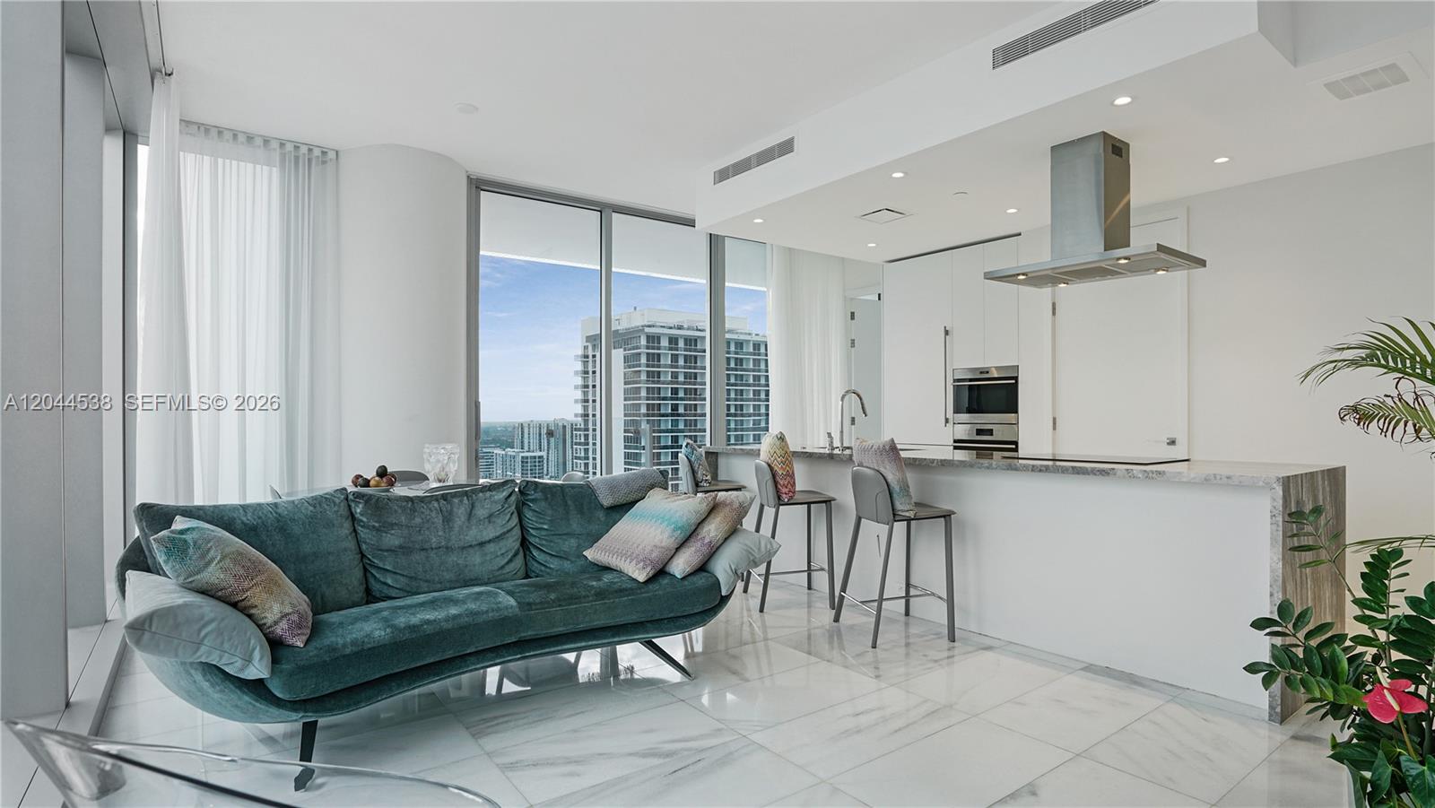 A modern living room and kitchen area feature marble floors, a teal sofa, and city views — 700 NE 26th Ter # 3005, Miami FL 33137, MIAMI, FL