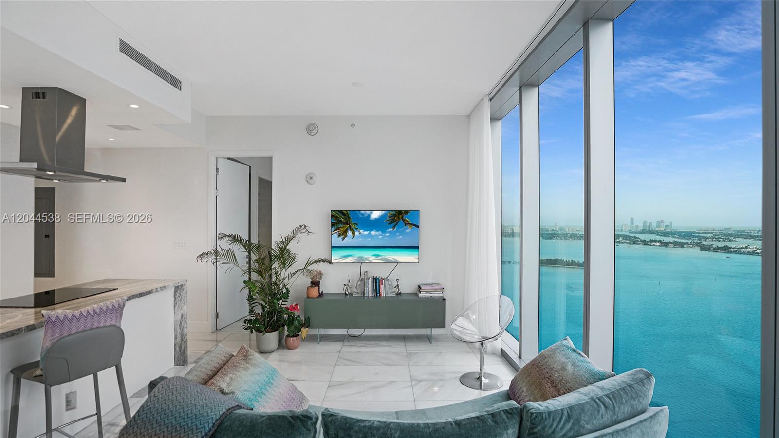 A modern living room features marble floors, a wall-mounted television, and floor-to-ceiling bay views — 700 NE 26th Ter # 3005, Miami FL 33137, MIAMI, FL