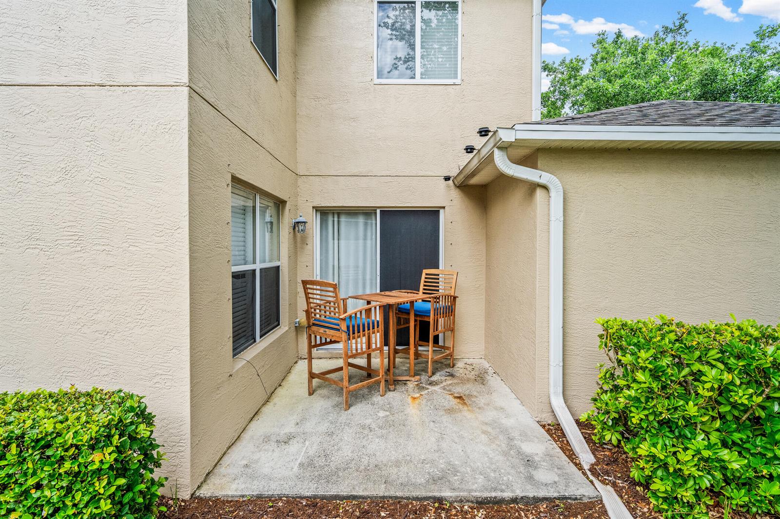 A small concrete patio with a wooden bistro set sits outside a tan stucco building — 1814 Pointe West Way, Vero Beach FL 32966, VERO BEACH, FL