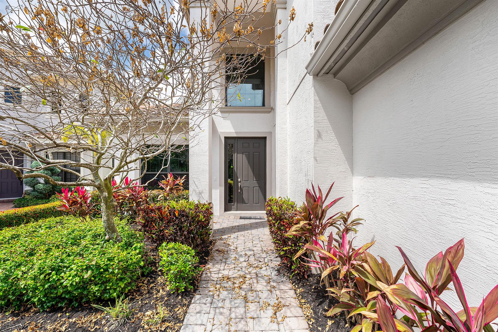 A paved walkway leads to the front entrance of a white stucco house with landscaping — 10175 Cameilla Street, Parkland FL 33076, PARKLAND, FL