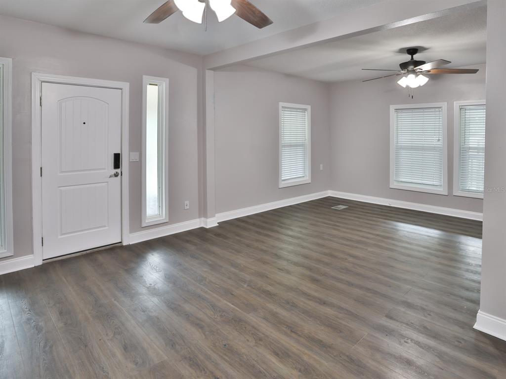 An empty living room features gray walls, wood-look flooring, two ceiling fans, and a front door — 3016 N MARYLAND AVENUE, PLANT CITY, FL