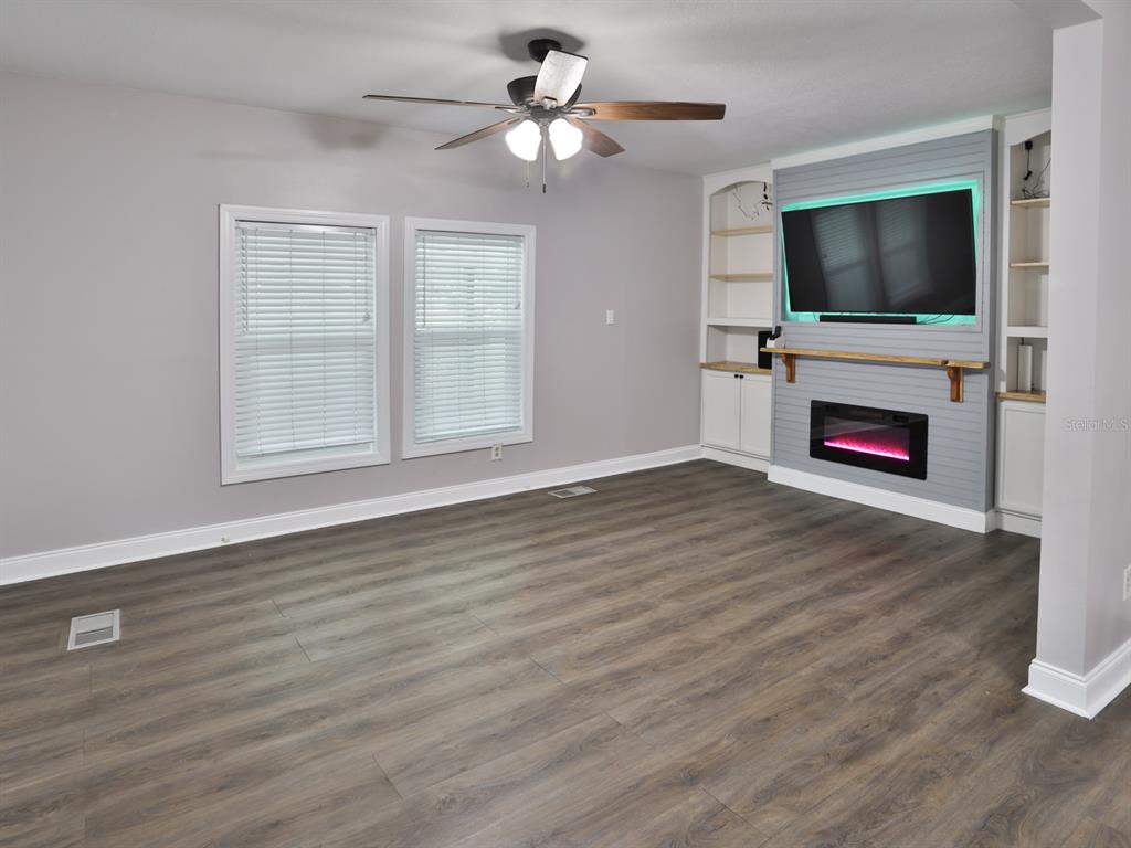 A living room features wood-look flooring, a ceiling fan, and a fireplace with built-in shelving — 3016 N MARYLAND AVENUE, PLANT CITY, FL